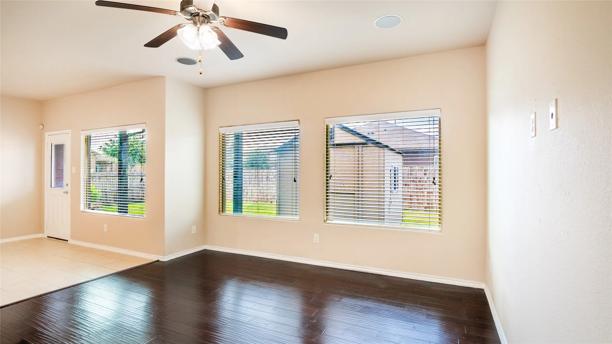 Spacious room featuring dark wood-finish flooring, light-toned wall paint, multiple windows with blinds, a ceiling fan, and recessed lighting