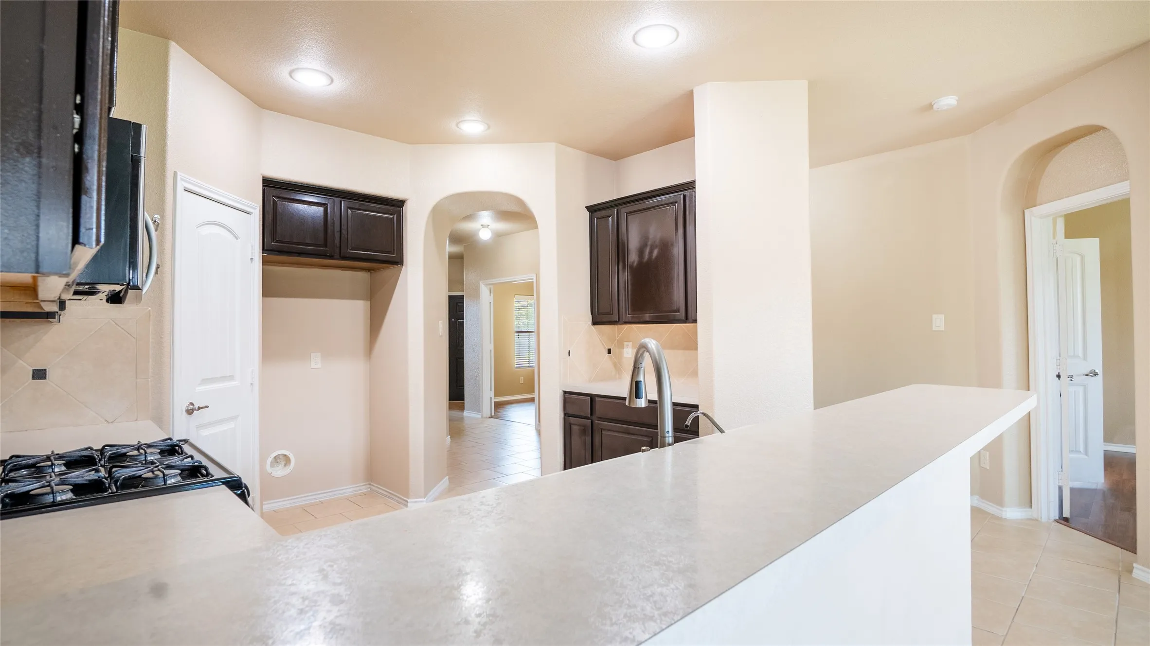 Kitchen featuring a gas range, dark wood-finish cabinetry, light-toned countertops, and recessed lighting