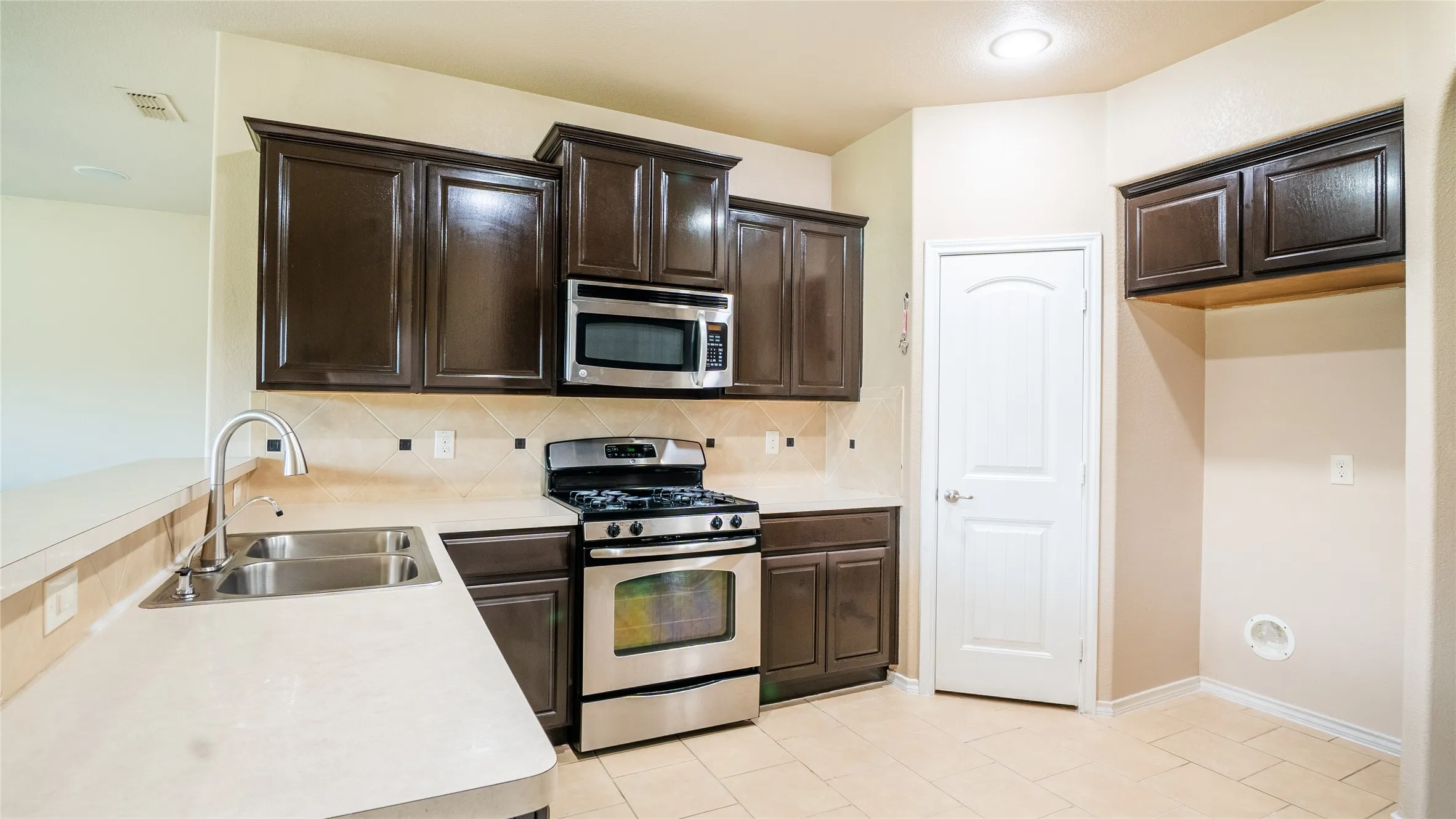 Kitchen featuring dark wood cabinetry, stainless steel appliances, a double basin sink, light-toned countertops, and tile flooring