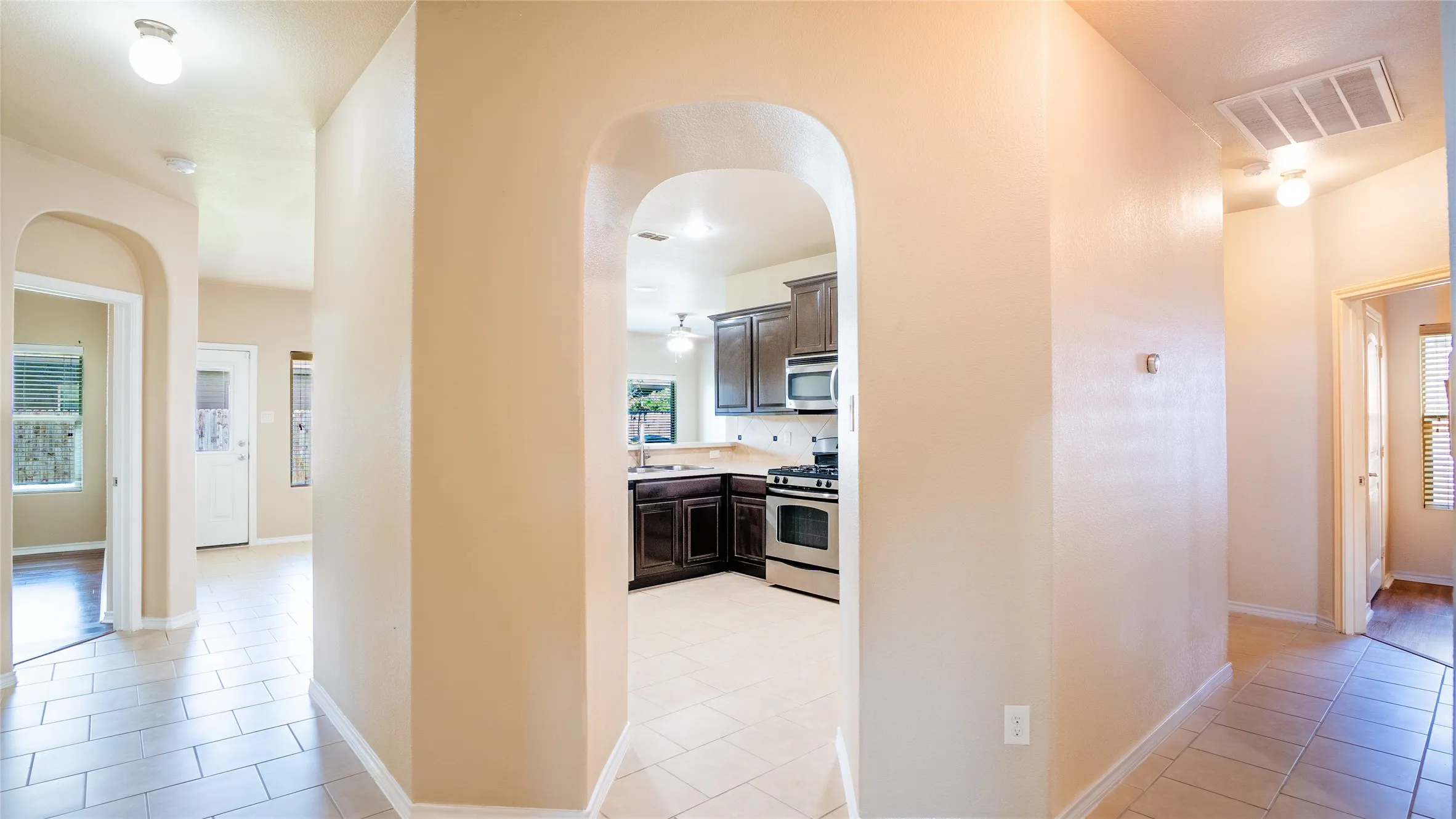 Arched hallways with tile flooring, dark wood-finish cabinetry, stainless steel appliances, and a built-in oven