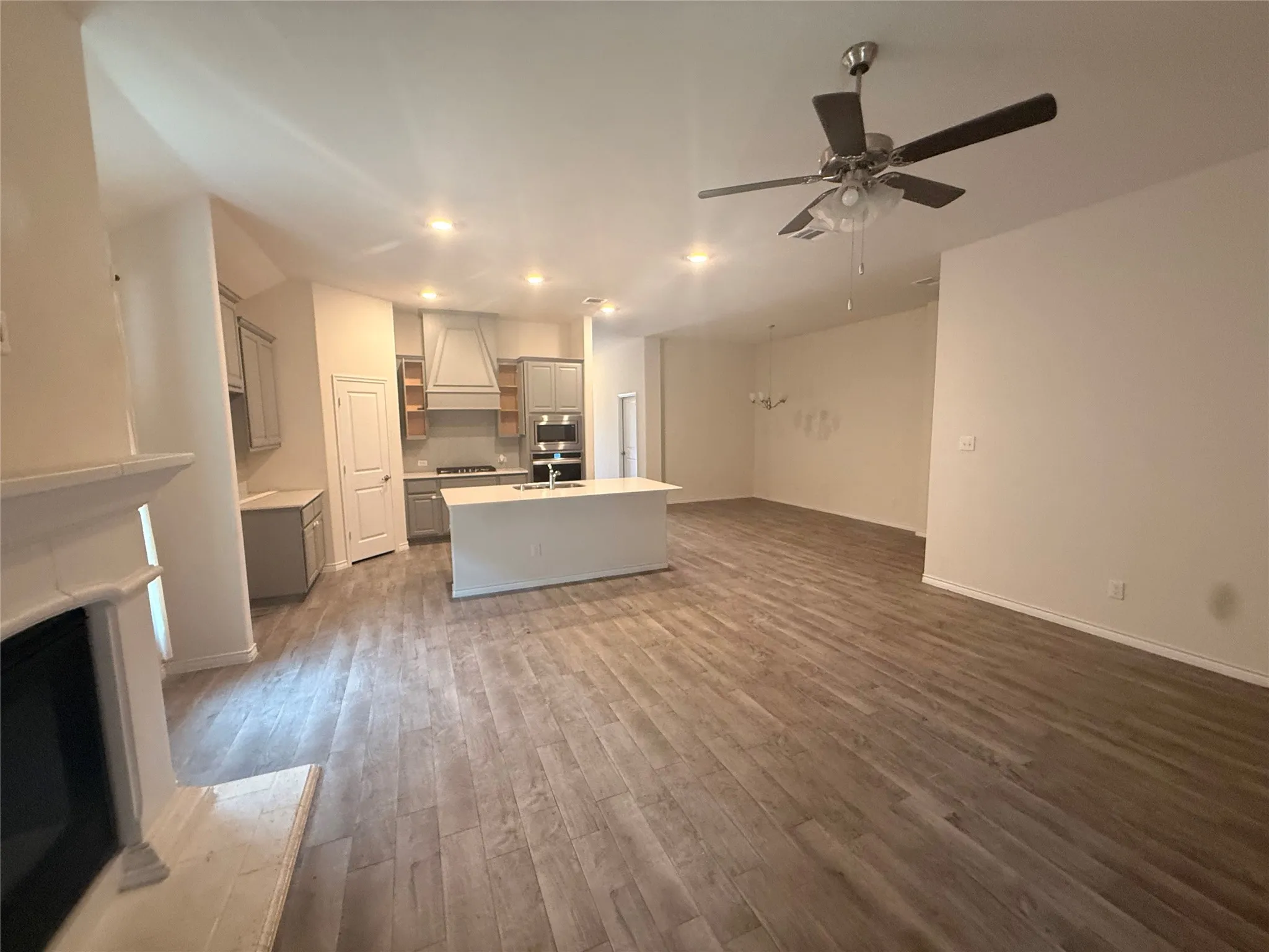 Open-concept living area with wood-finish flooring, a fireplace, and an integrated kitchen featuring an island with a sink and built-in appliances