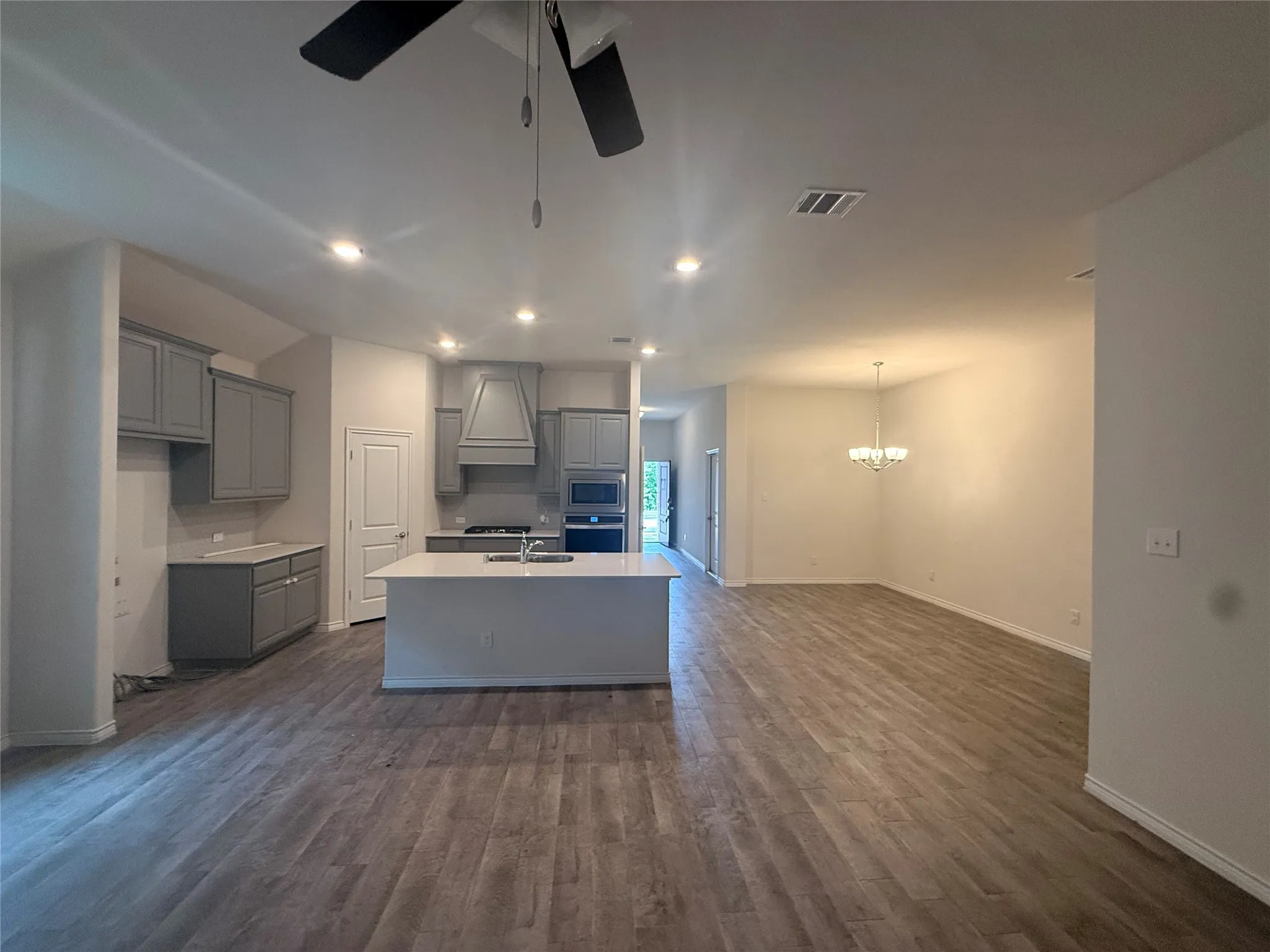 Open-concept living space with wood-finish flooring, recessed lighting, a ceiling fan, and a kitchen island with sink