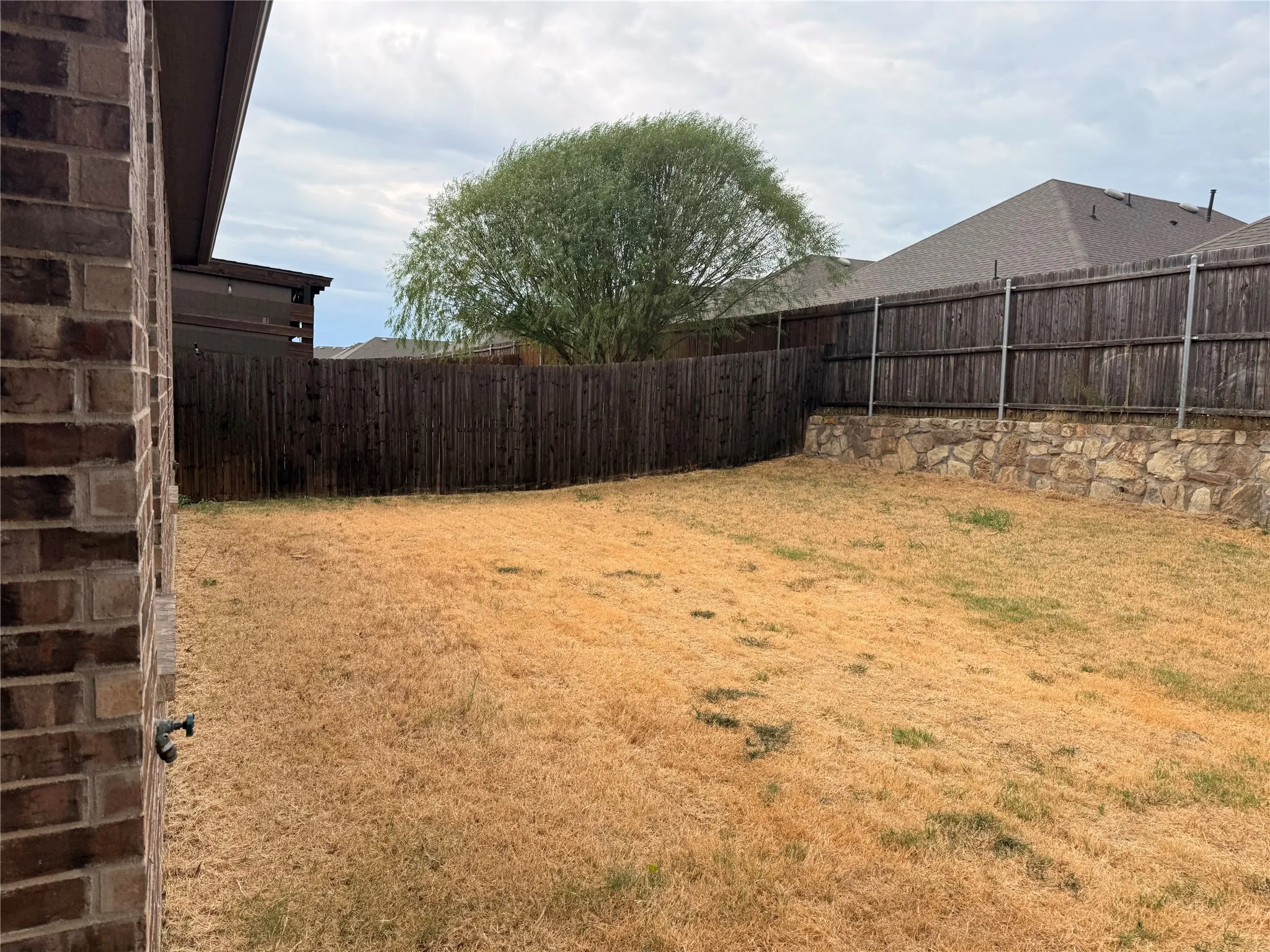Expansive yard featuring a wooden fence, a stone retaining wall, and a mature tree