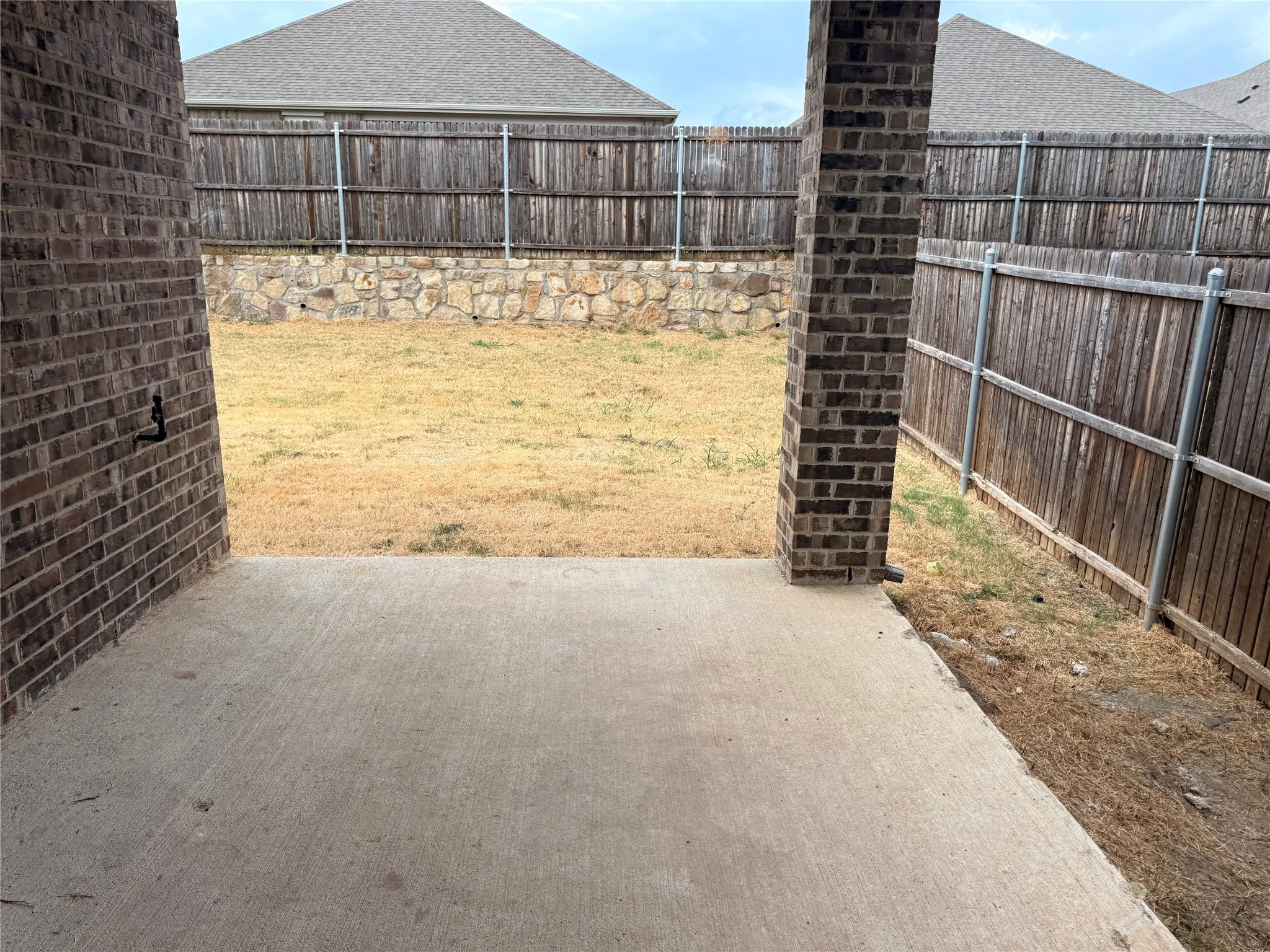 Concrete patio area with brick support columns, wood fencing, and a stone retaining wall