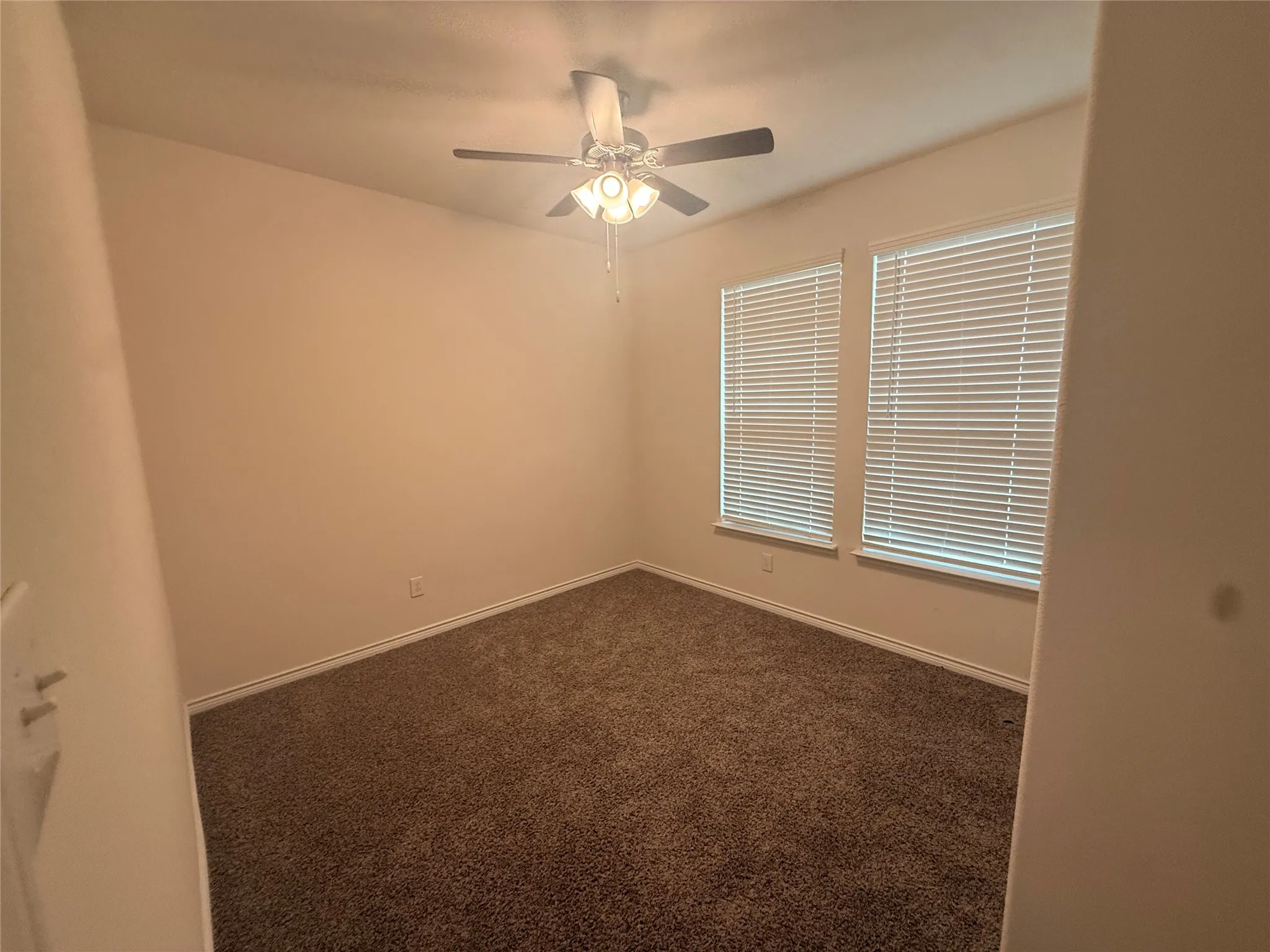 Wall-to-wall carpeting, ceiling fan with integrated lighting, and two windows with horizontal blinds