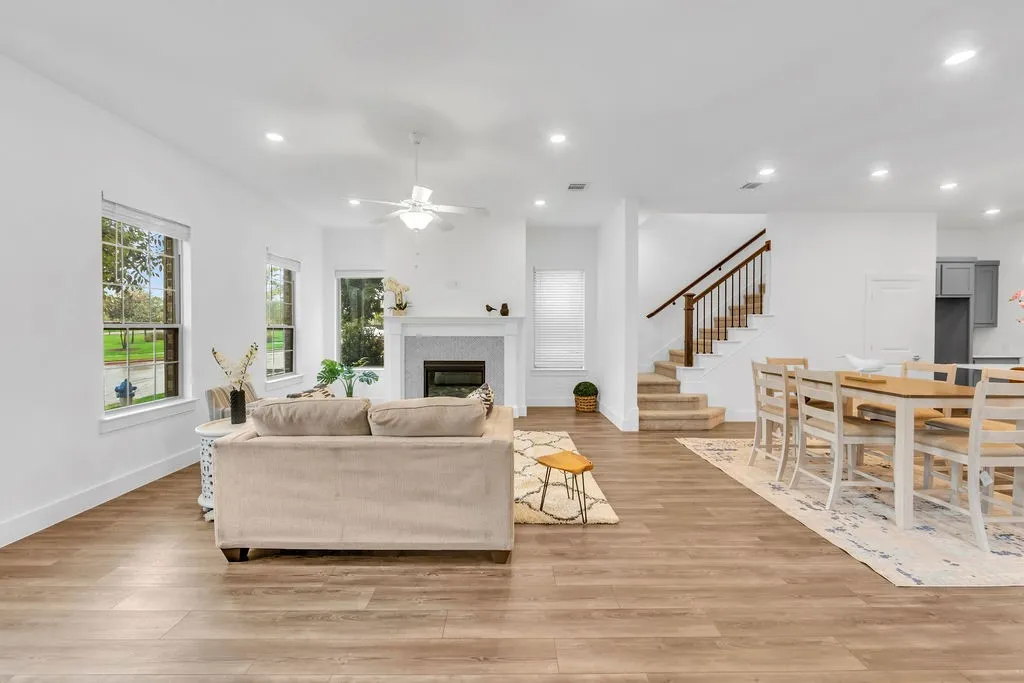 Wood-finish flooring throughout, white walls, recessed lighting, fireplace with mantel, and a staircase with wood handrails