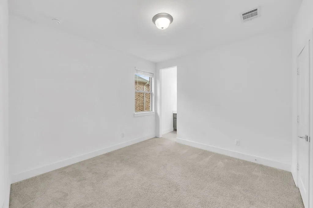 Light gray wall-to-wall carpeting, single window with white trim, flush mount ceiling light fixture, white interior door with polished nickel hardware, and an open doorway