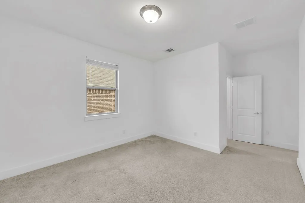 White walls with light-colored carpeting, featuring a window with blinds, a ceiling-mounted light fixture, and a paneled interior door