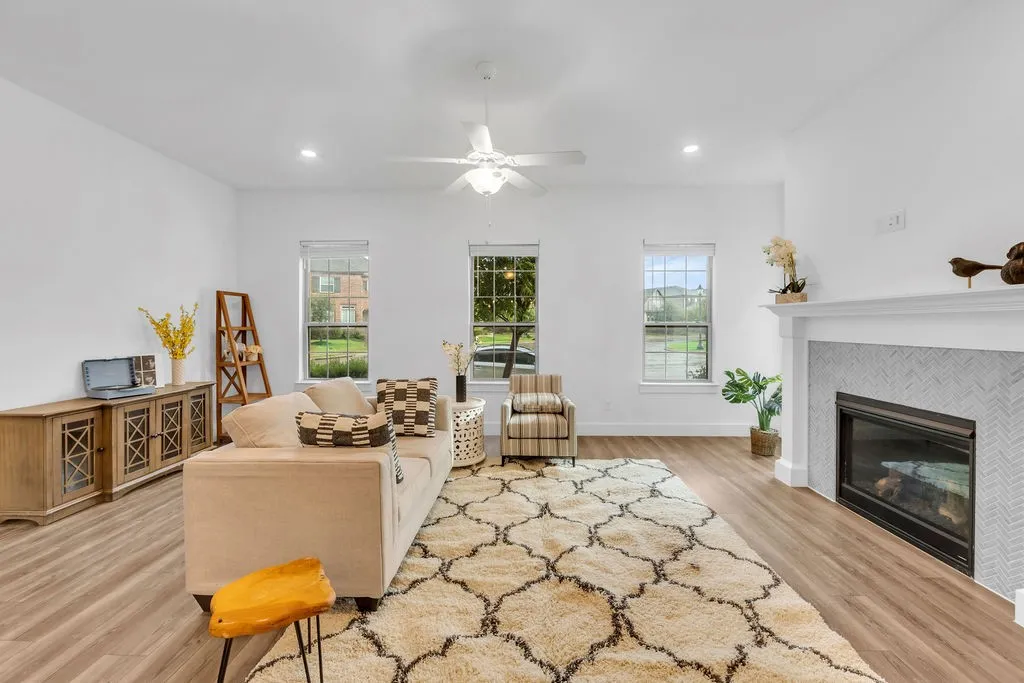 Recessed lighting, wood-finish flooring, white ceiling fan, multiple windows, and a built-in fireplace with a tile surround and mantel