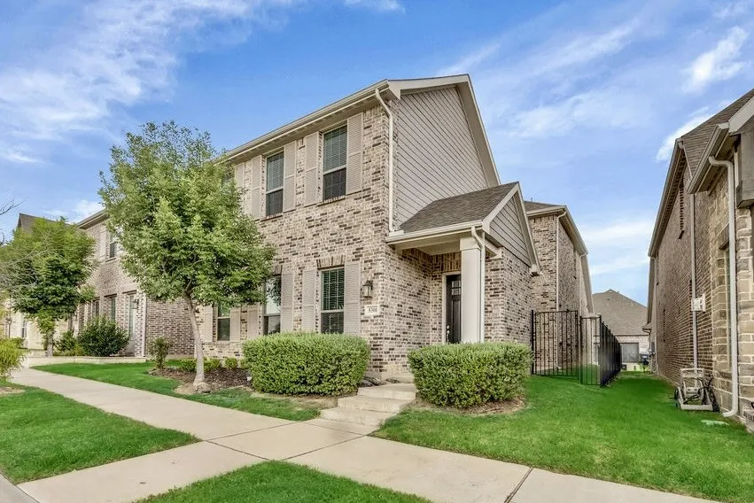 Brick facade with shuttered windows, covered entryway, established shrubs, and a side fence