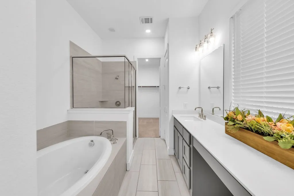 Dual vanity with undermount sinks, a built-in bathtub, a walk-in shower with glass enclosure, and light-toned tile flooring