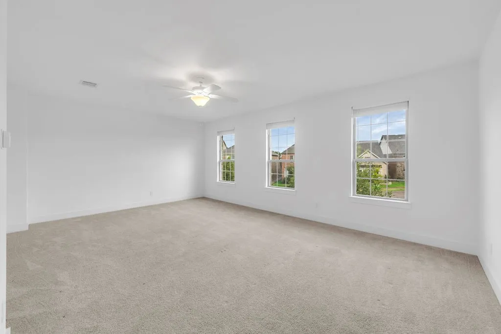 Expansive room featuring three windows, a ceiling fan with integrated lighting, and neutral-toned carpeting