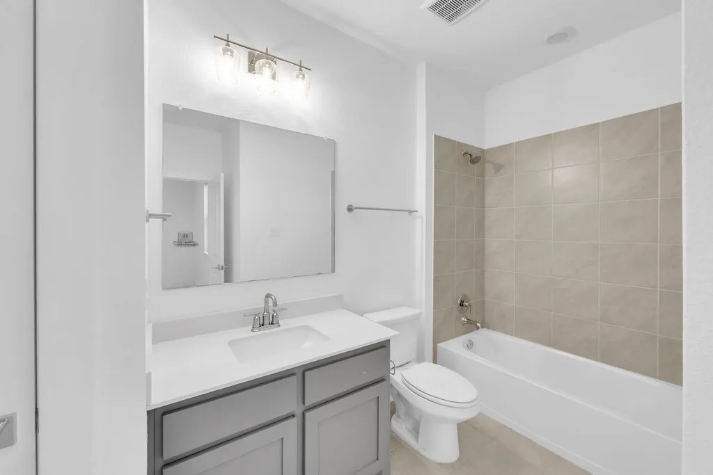 Vanity with gray cabinetry and white countertop, undermount sink with chrome faucet, framed mirror, and three-light fixture