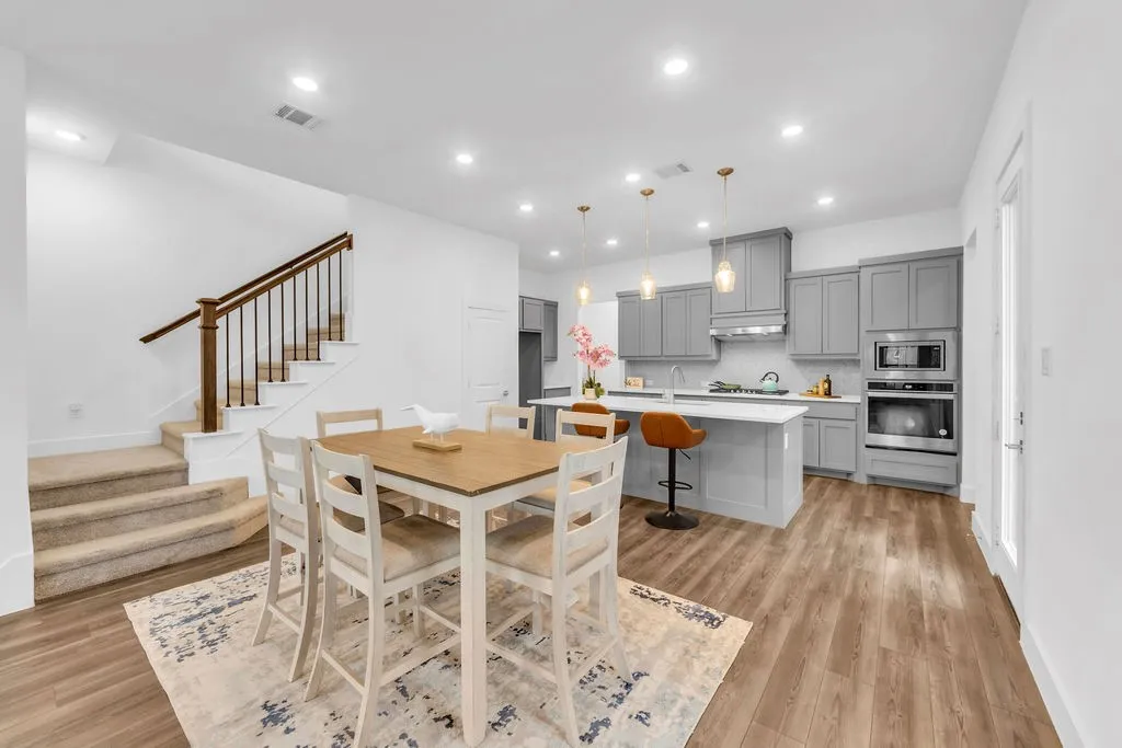 Open-concept layout featuring wood-finish flooring, a kitchen with gray cabinetry, stainless steel appliances, a white island with seating, and recessed lighting