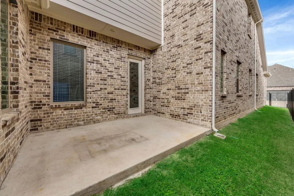 Concrete patio with a brick exterior, single-pane door, and multiple windows with blinds