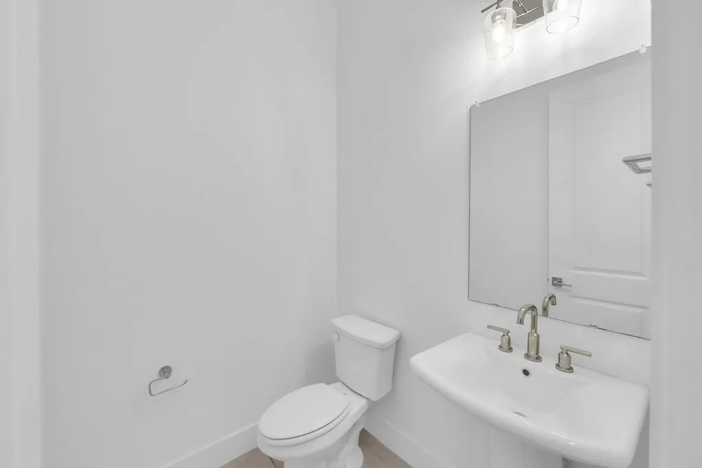 Pedestal sink with a brushed nickel faucet, wall-mounted mirror, and overhead vanity lighting