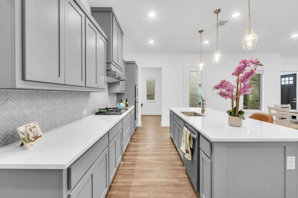 Light gray cabinetry with a herringbone tile backsplash, white countertops, and wood-finish flooring