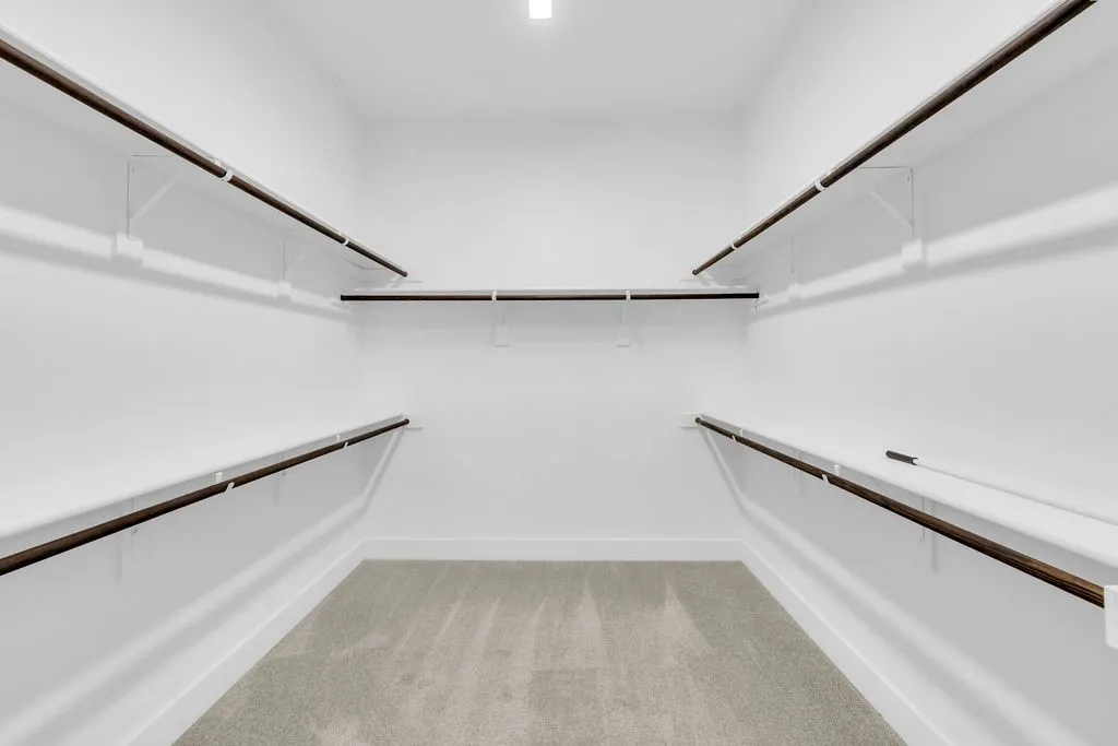 Spacious walk-in closet with extensive shelving, multiple hanging rods, and light gray carpeting