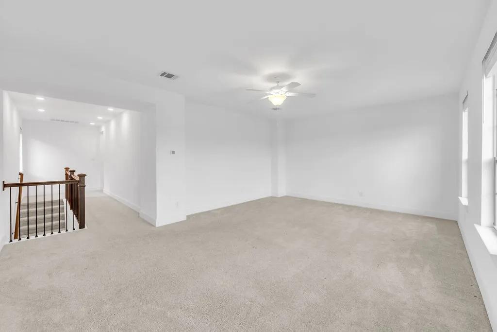 Expansive carpeted area with bright neutral walls and a ceiling fan