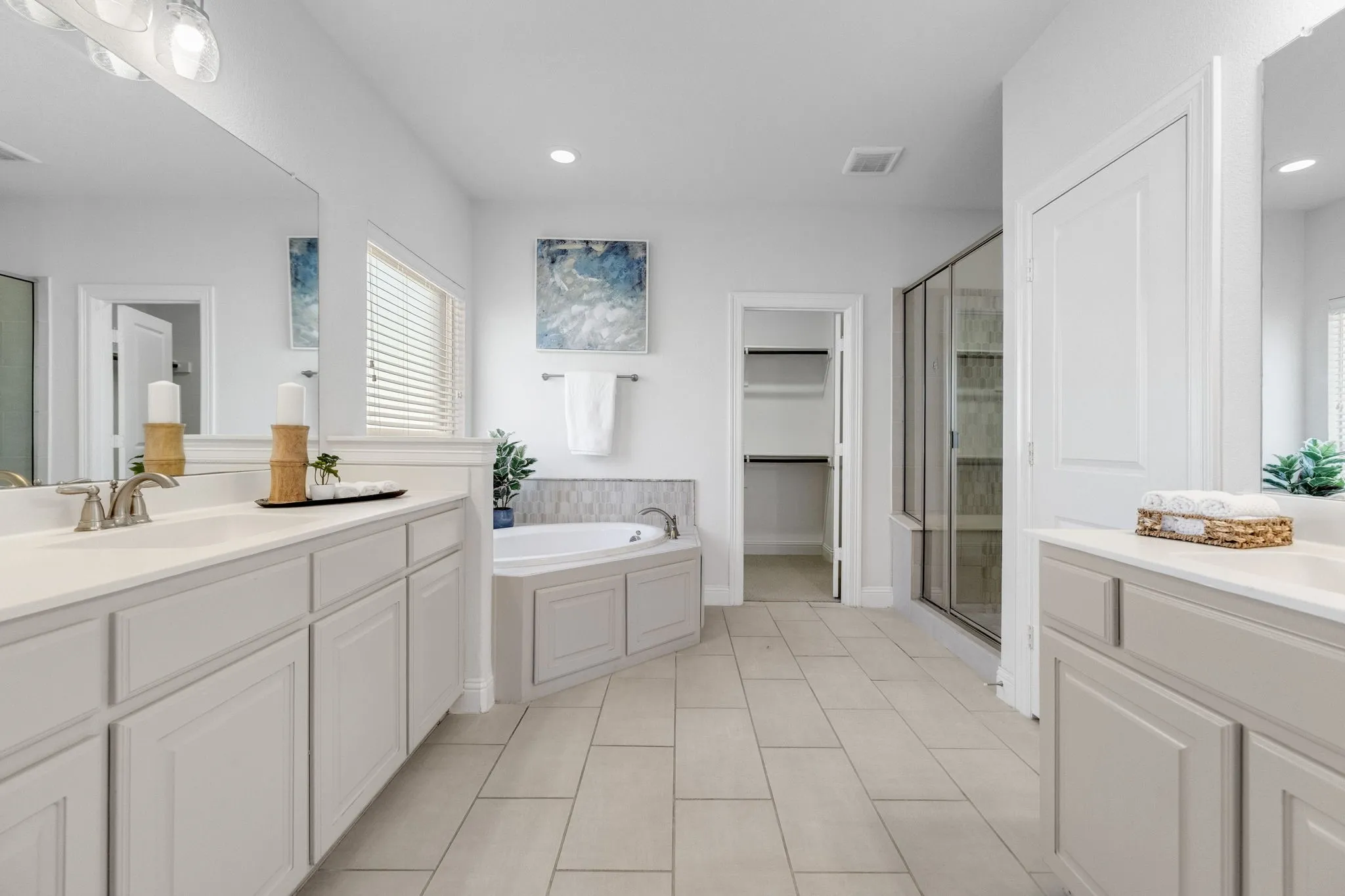 Dual vanity with white countertops, built-in soaking tub, glass-enclosed shower, walk-in closet, and tiled flooring