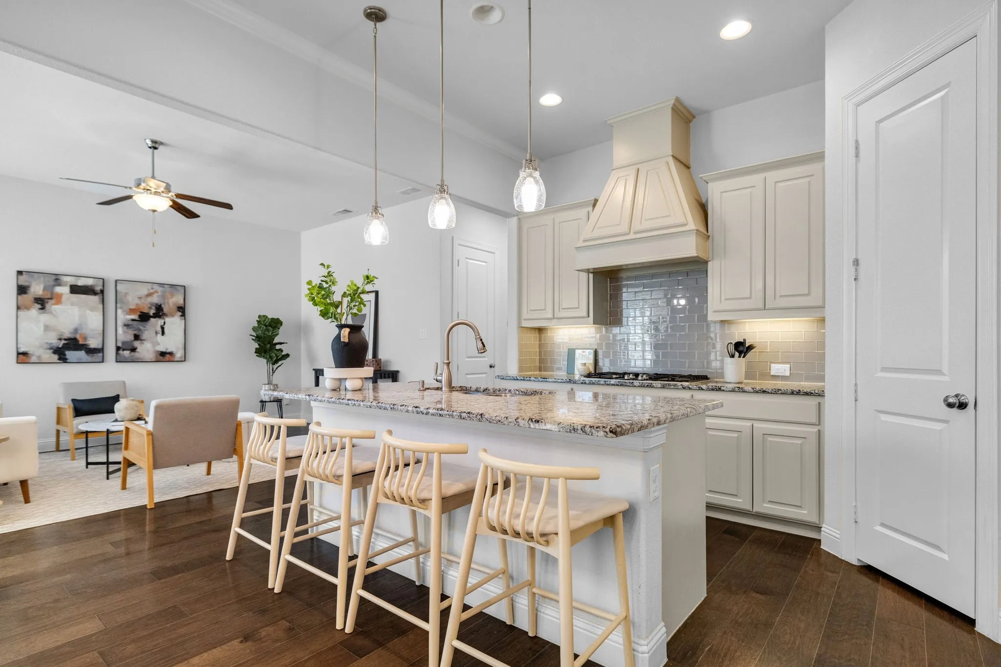 Kitchen island with a granite countertop, white cabinetry, decorative range hood, subway tile backsplash, and wood-finish flooring