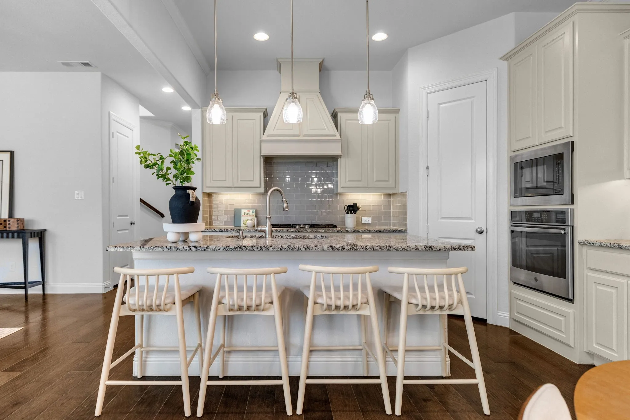 Kitchen with a central island featuring a granite countertop, pendant lighting, built-in stainless steel appliances, and wood-finish flooring