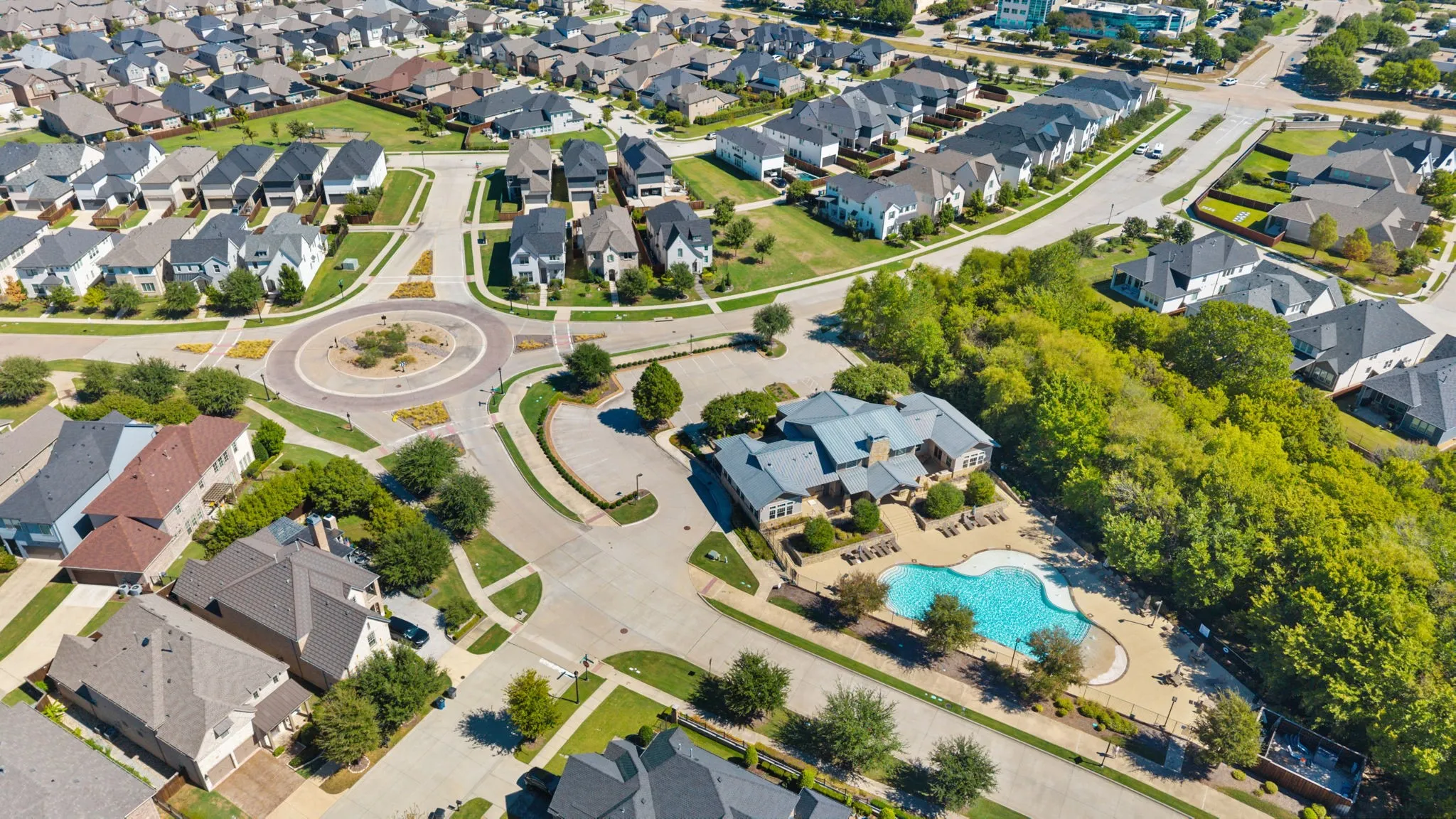 Community featuring a central roundabout, extensive green spaces, and a shared swimming pool with surrounding patio