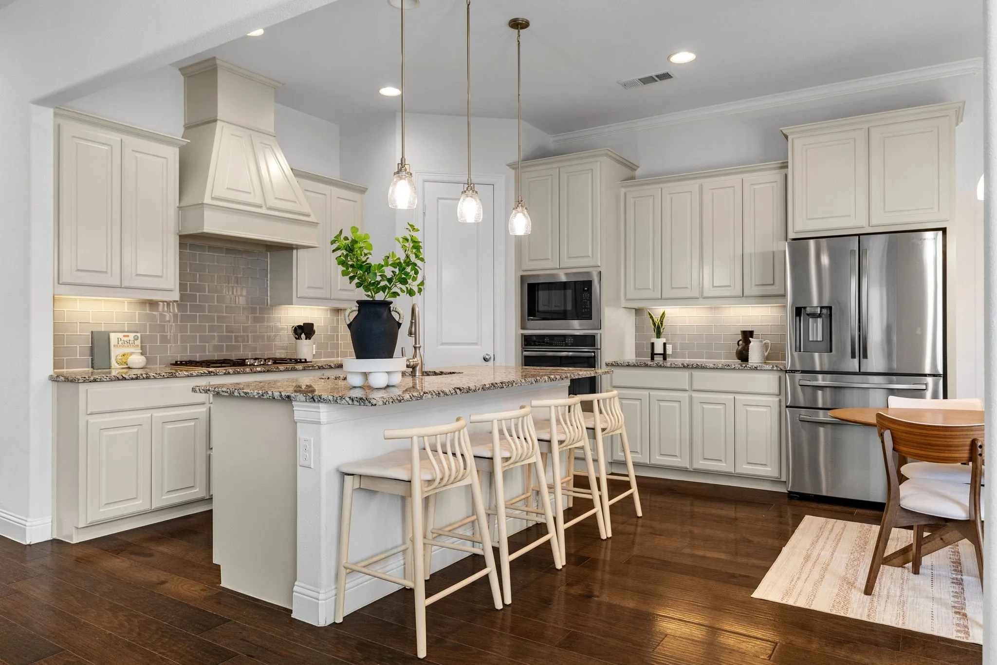 Kitchen featuring wood-finish flooring, an island with countertop seating, stainless steel appliances, light-toned cabinetry, and pendant lighting