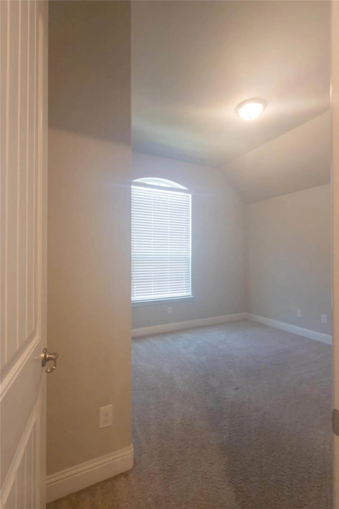 Arched window with blinds, recessed ceiling, flush mount lighting, and gray carpet flooring