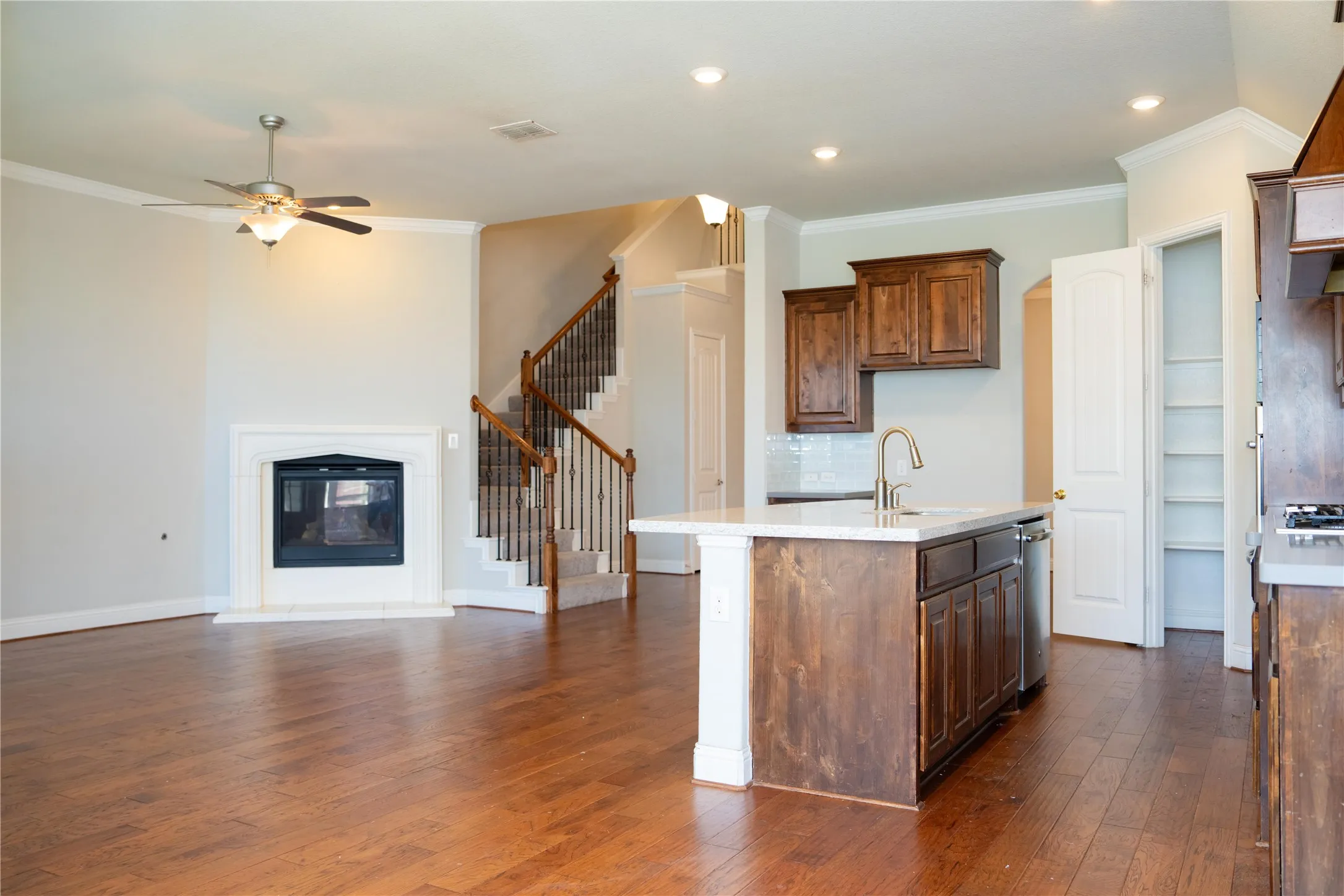 Open-concept living area featuring wood-finish flooring, a white-mantled fireplace, and a ceiling fan