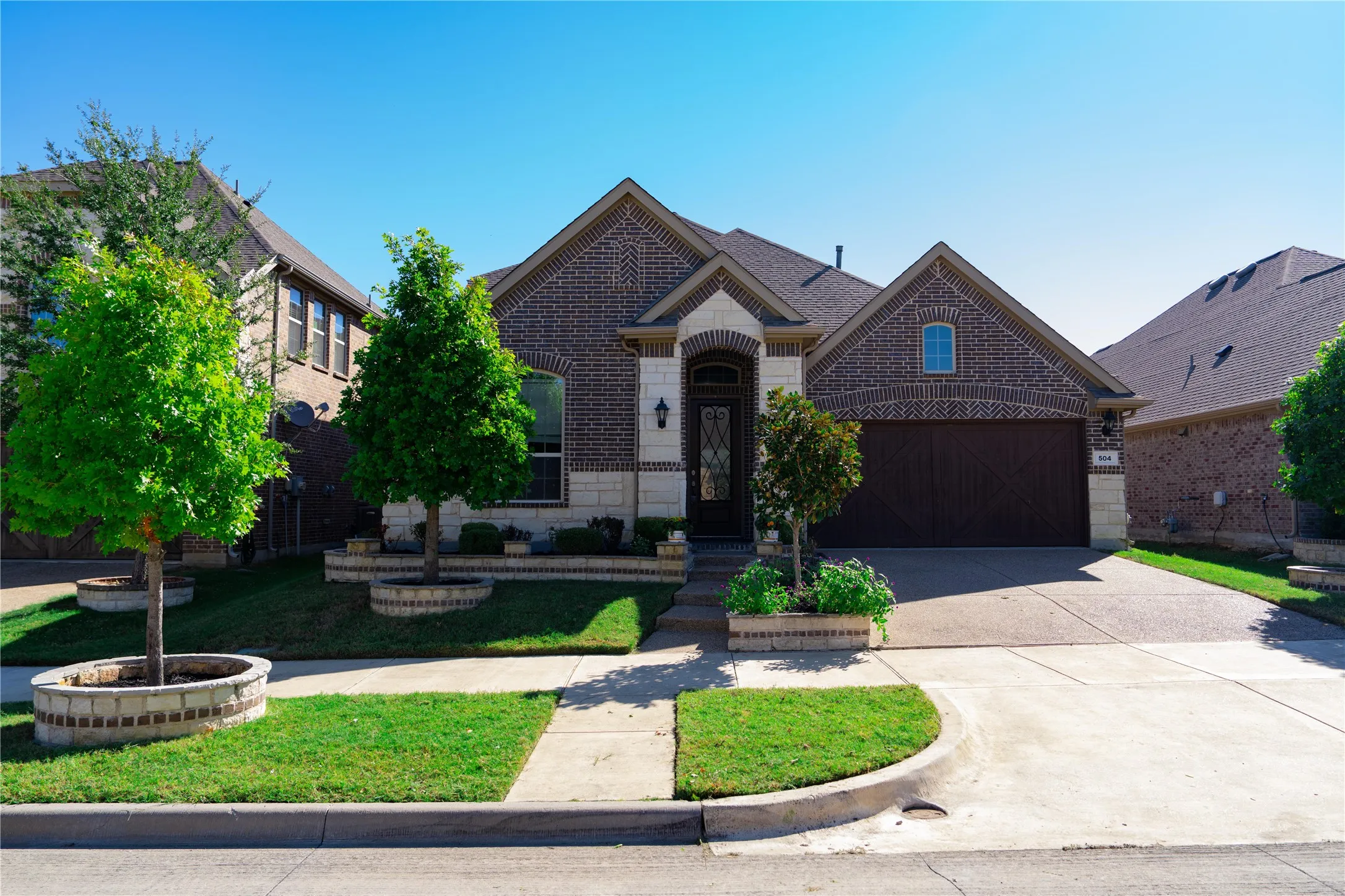 Brick and stone exterior with an arched entryway, decorative garage door, and mature landscaping