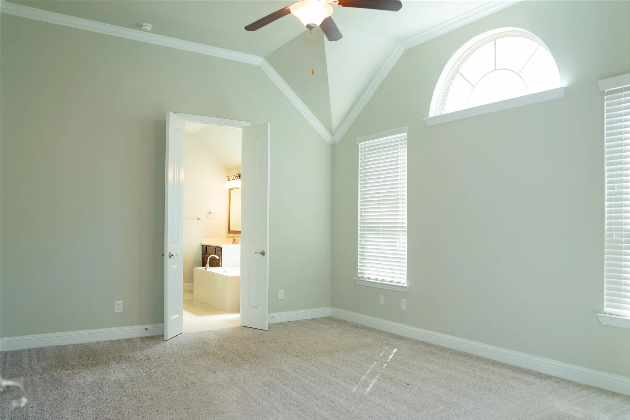 Vaulted ceiling, ceiling fan, arched transom window, two vertical windows with blinds, and light-toned carpet flooring
