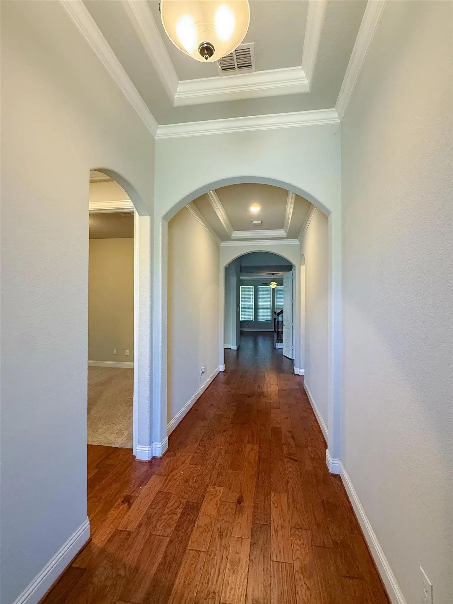 Hardwood flooring throughout, tray ceiling with crown molding, and arched doorways