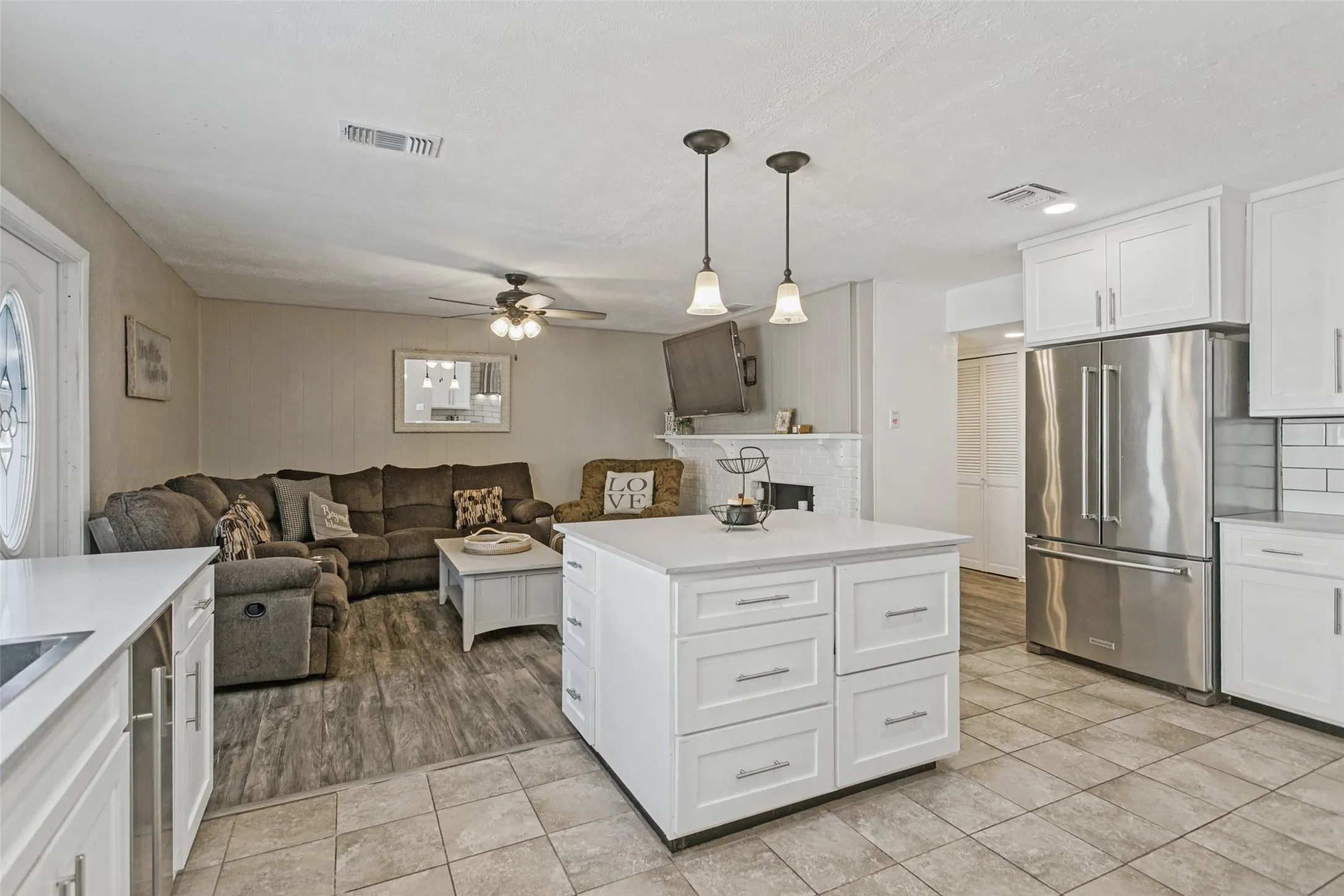 Updated kitchen featuring white shaker cabinetry, stainless steel refrigerator, white subway tile backsplash, and a central island with pendant lighting