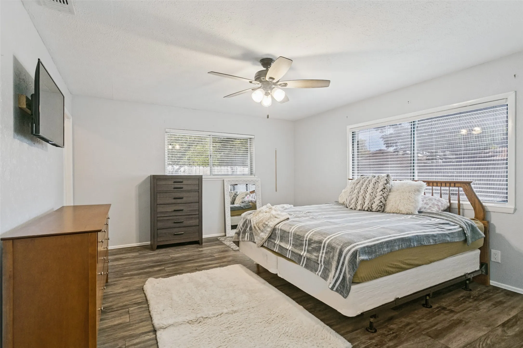 Wood-finish flooring, ceiling fan with integrated lighting, two windows with blinds, and white painted walls