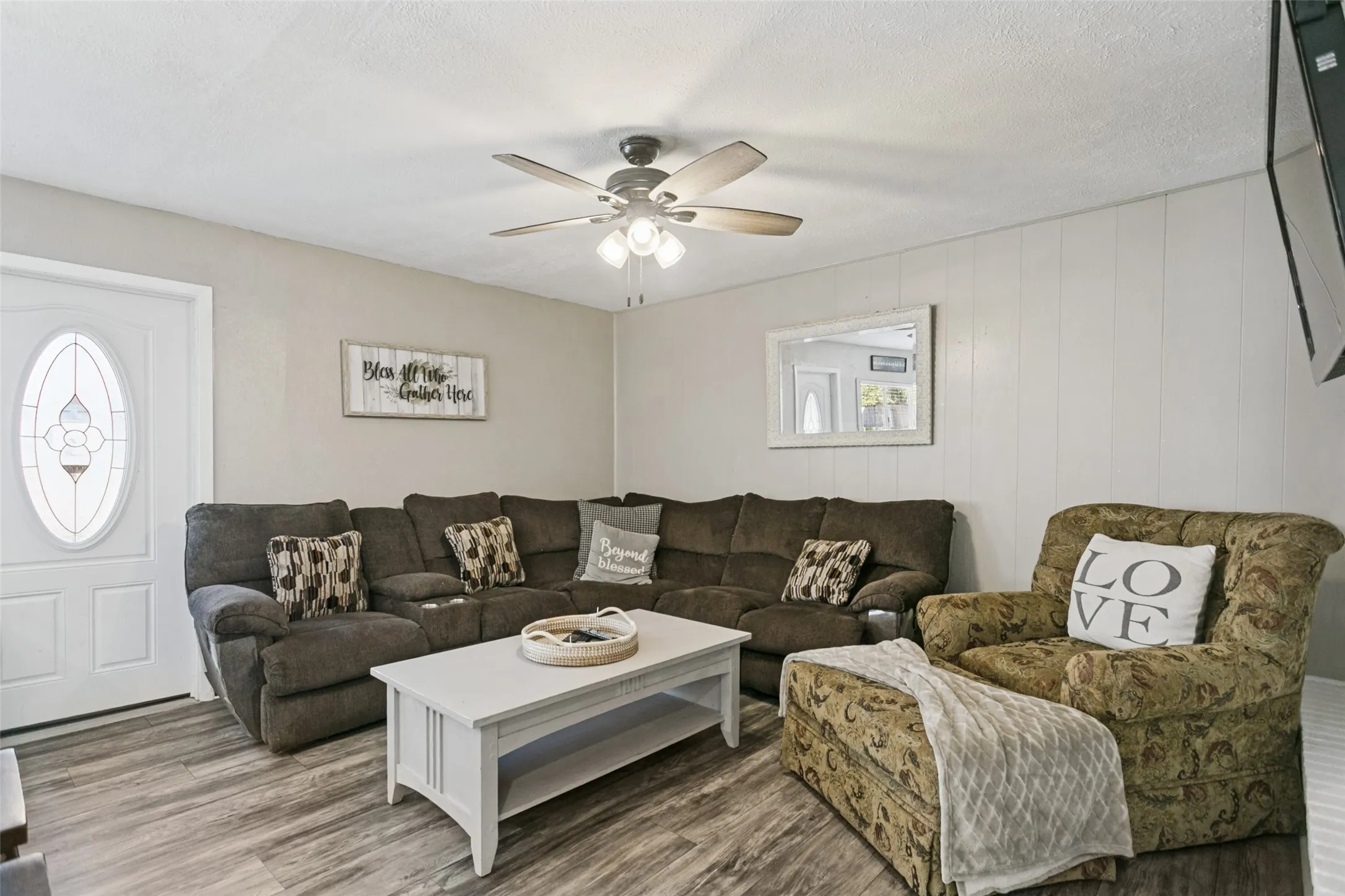 Wood-finish flooring, white paneled wall, ceiling fan with integrated lighting, white entry door with decorative glass insert, and neutral wall paint