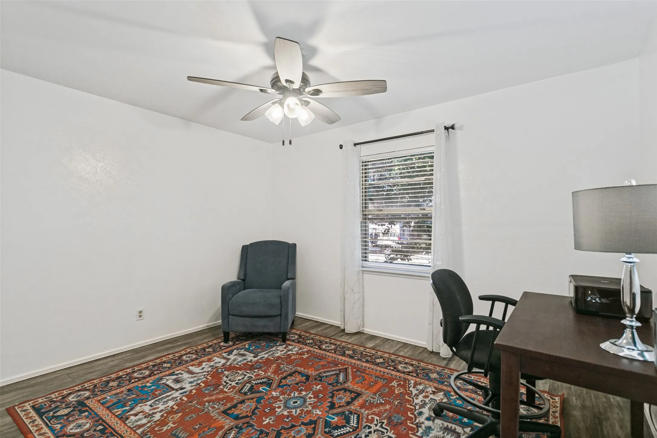 Wood-finish flooring, white walls, window with blinds, and a ceiling fan with integrated lighting