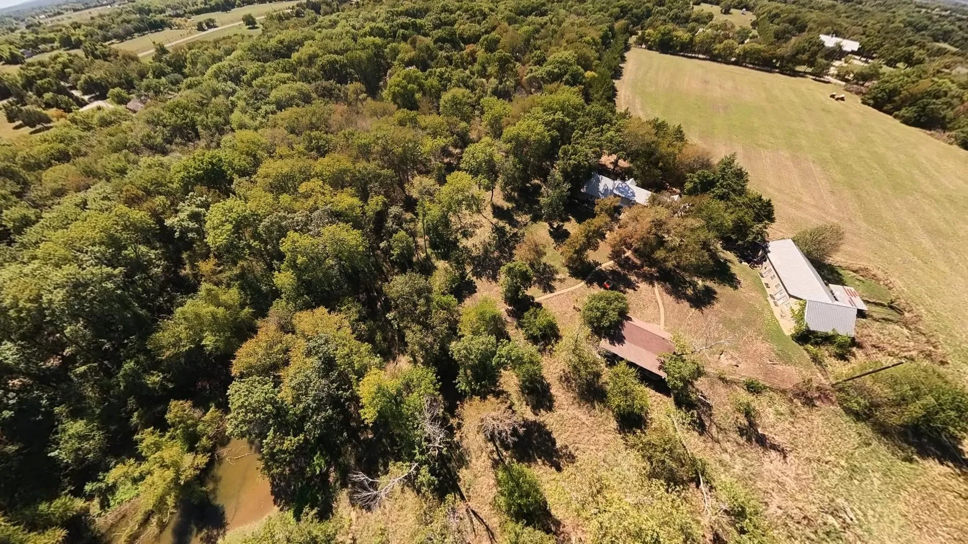 Expansive wooded acreage featuring a visible creek, multiple structures, and open land