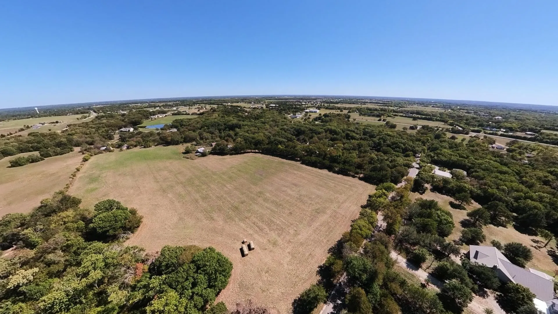 Expansive landscape featuring open fields, mature trees, and a clear blue sky
