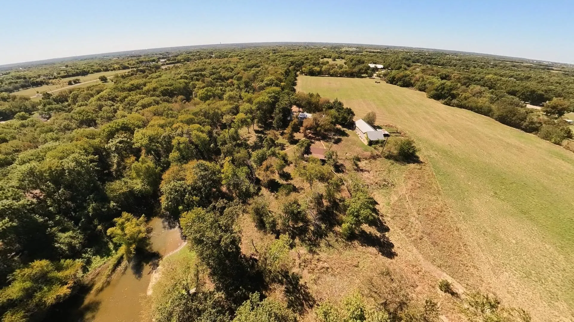 Expansive acreage featuring a body of water, mature tree coverage, open fields, and a barn structure