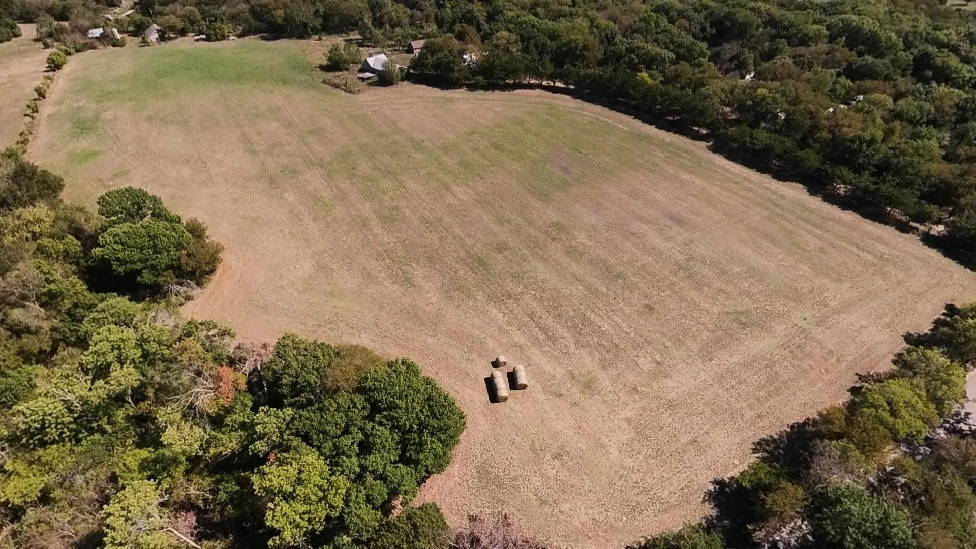 Expansive cleared land featuring two hay bales and surrounded by mature trees