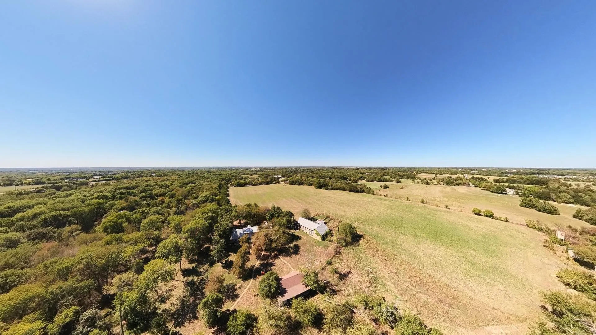 Expansive rural landscape featuring a mix of mature trees, open fields, and residential structures