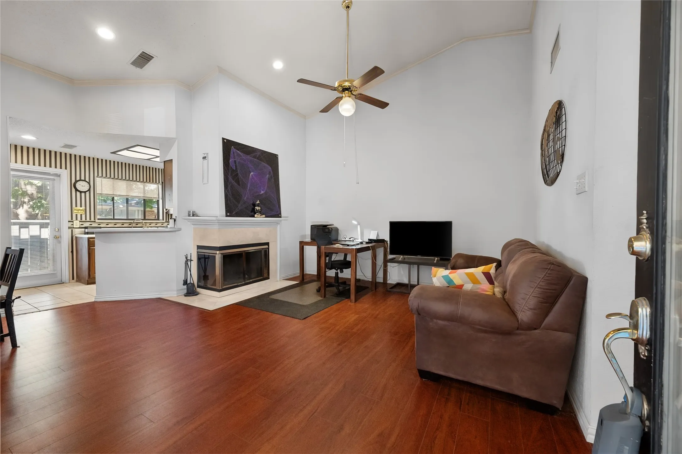 Vaulted ceiling with a ceiling fan, wood-finish flooring, built-in fireplace, and a pass-through kitchen opening