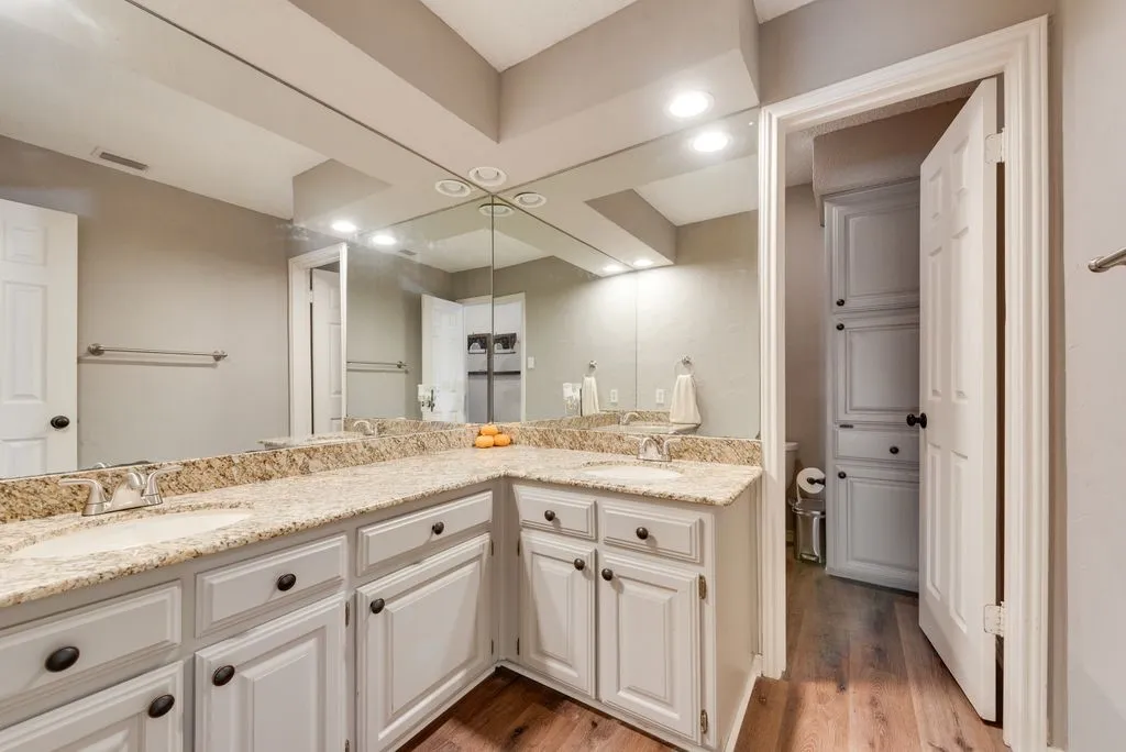 Dual vanity with integrated sinks, light-toned countertops, white cabinetry with dark hardware, and wood-finish flooring