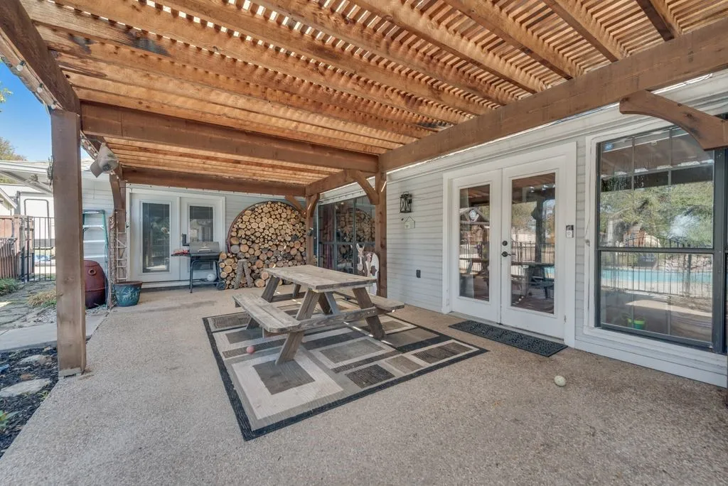 Expansive concrete patio with a wooden pergola, double French doors, large window, and light-colored siding