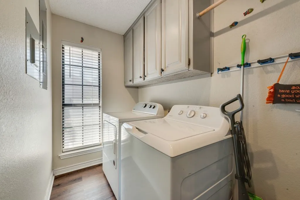 Laundry area featuring wood-finish flooring, overhead cabinetry, and a window with blinds