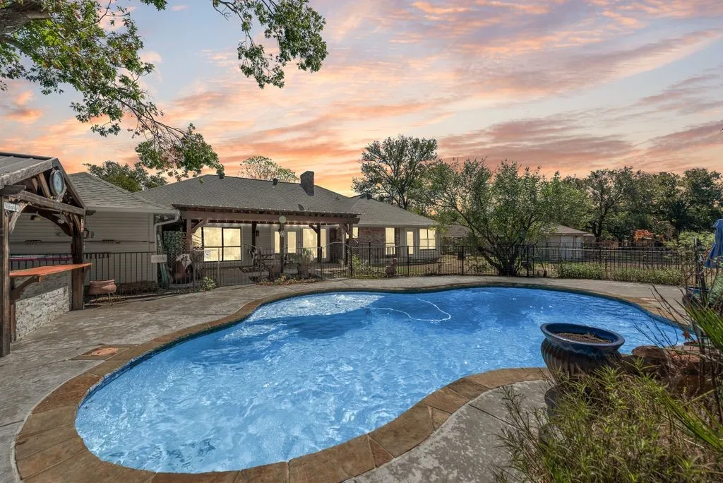 In-ground swimming pool with a sculpted edge, extensive concrete decking, a built-in pergola, and a covered outdoor bar area