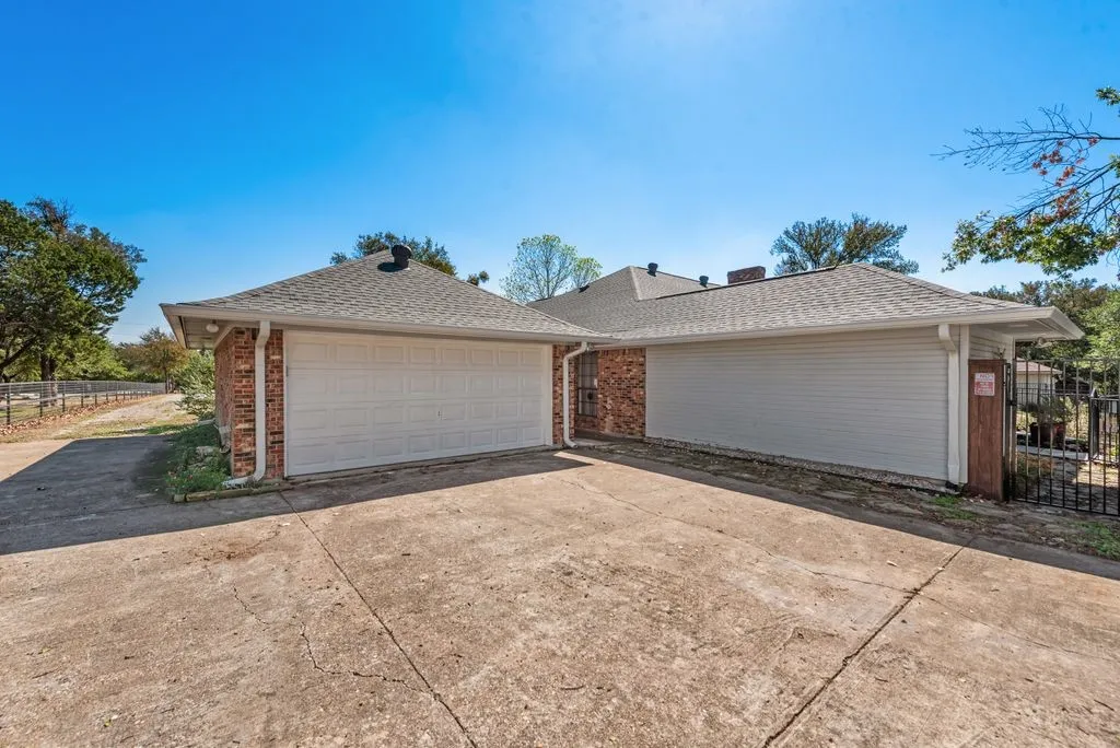 Exterior featuring brick siding, a light-colored shingle roof, white garage door, and a concrete driveway