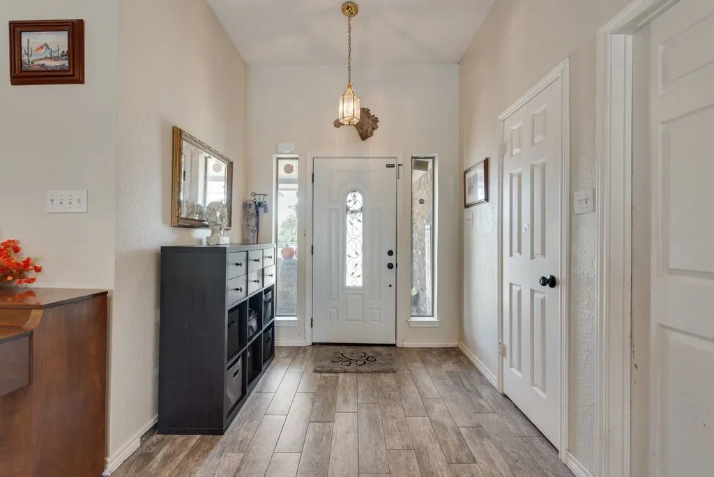 Vaulted entry with wood-finish flooring, white paneled entry door, two sidelight windows, and a hanging brass-finish light fixture