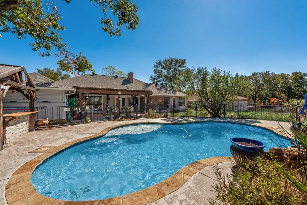 Freeform pool with a stone coping, stamped concrete patio, and a built-in outdoor bar
